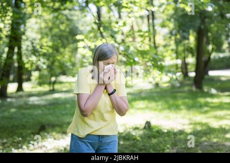 Saisonale Allergien. Eine ältere Frau im Park hat in der Natur Atembeschwerden, nutzt einen Inhalator. Niest und hustet in ein Taschentuch. Hat alle Stockfoto