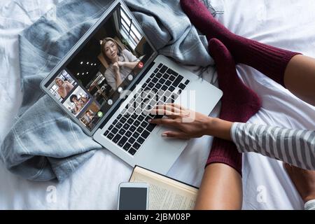 Junge Frau Videokonferenzen mit Kollegen aus verschiedenen Rassen durch Laptop auf dem Bett zu Hause. Unverändert, Geschäft, Freiberufler, drahtlose Technologie, teamwo Stockfoto