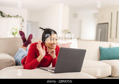 Lächelnde Biracial junge Frau winkt Hand während Videoanruf auf Laptop zu Hause Stockfoto