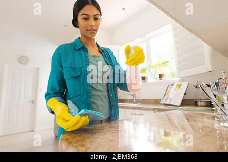 Biracial junge Frau trägt Handschuhe Reinigung Küchentisch zu Hause Stockfoto