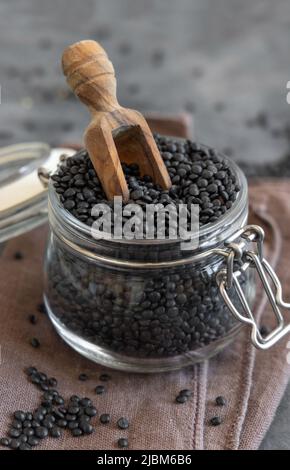 Glas mit trockenen schwarzen Linsen Bohnen mit einer Holzlöffel auf dem grauen Tisch aus nächster Nähe. Gesunde Ernährung, Proteinquelle für vegane und vegetarische Ernährung. Tradi Stockfoto