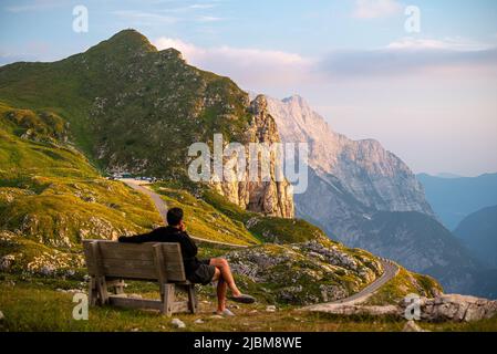 Einsamer Wanderer, der sich auf einer Holzbank entspannt und den großartigen Blick auf den Mangart-Berg im Triglav-Nationalpark, den Julischen alpen, genießt Stockfoto