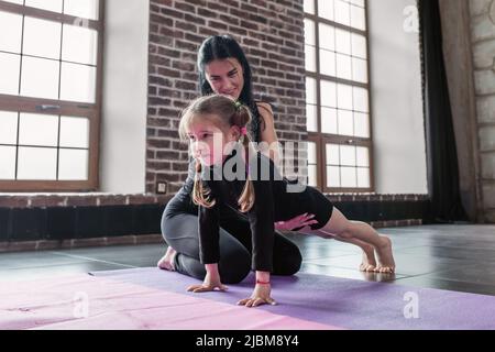 Lächelnde Kinder Fitness-Trainer arbeitet mit einem kleinen Mädchen zeigen, wie man Plank-Übung im Fitness-Studio zu tun. Stockfoto