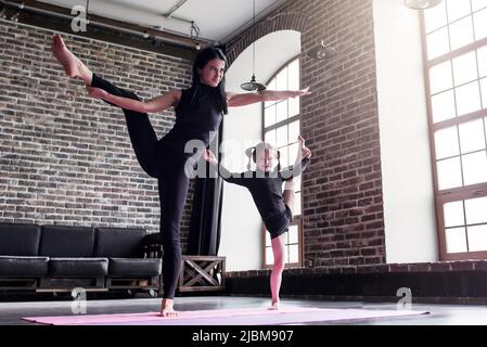 Mutter und kleine Tochter tun stehend gespaltene Bein Dehnung Übung halten Gleichgewicht. Stockfoto