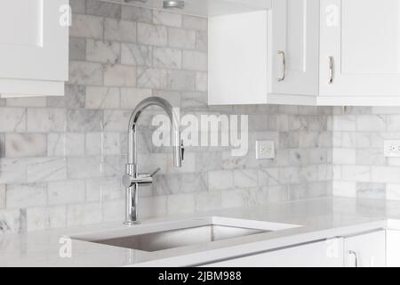 Ein Küchenwaschbecken Detail mit weißen Schränken und einer marmornen U-Bahn-Fliese backsplash aufgenommen. Stockfoto