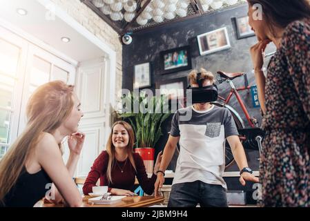 Eine Gruppe junger Leute, die Spaß miteinander haben, ein fröhlicher Mann, der in einem Café eine Brille trägt. Stockfoto
