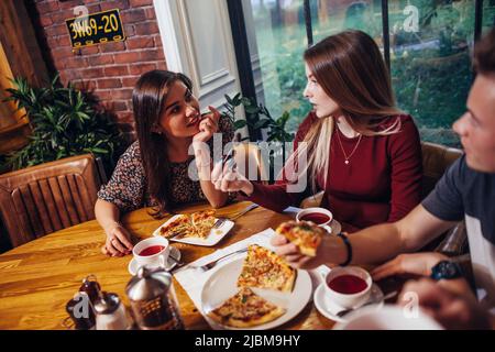 Freundinnen sind in ein Gespräch verwickelt, das Pizza im Café isst. Stockfoto