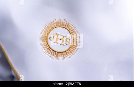 IHS christliches Symbol auf einem Kommunionskind. IHS Christogramm bestickt mit Goldfaden auf einer weißen Alba. Kleid der ersten Heiligen Kommunion. Stockfoto