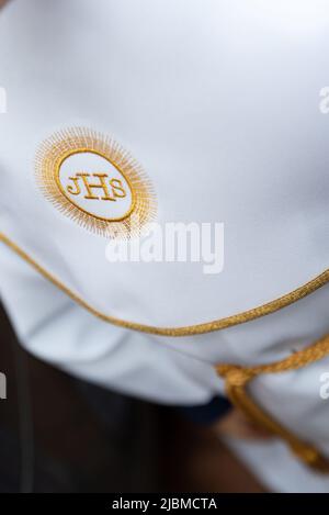 IHS christliches Symbol auf einem Kommunionskind. IHS Christogramm bestickt mit Goldfaden auf einer weißen Alba. Kleid der ersten Heiligen Kommunion. Stockfoto