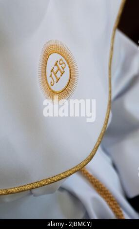 IHS christliches Symbol auf einem Kommunionskind. IHS Christogramm bestickt mit Goldfaden auf einer weißen Alba. Kleid der ersten Heiligen Kommunion. Stockfoto