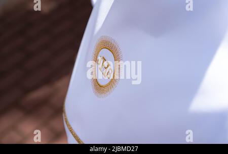 IHS christliches Symbol auf einem Kommunionskind. IHS Christogramm bestickt mit Goldfaden auf einer weißen Alba. Kleid der ersten Heiligen Kommunion. Stockfoto