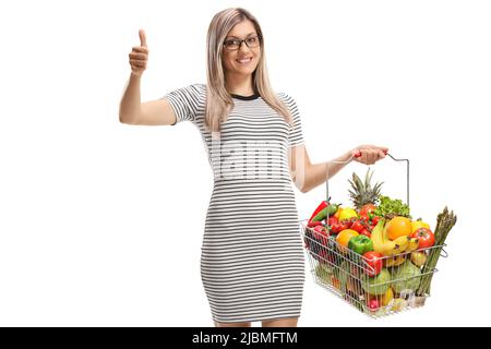 Frau mit einem Korb mit Obst und Gemüse, die ihre Daumen isoliert auf weißem Hintergrund zeigt Stockfoto