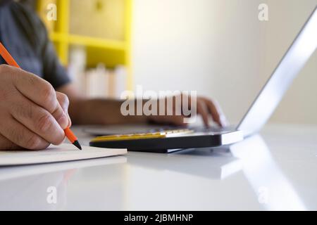 Verwenden Sie einen Laptop, Nahaufnahme der Verwendung eines Laptops und Notizen in einem Notebook. Fokussierter Mitarbeiter Mitarbeiter, der online arbeitet oder Meetings oder Schulungen absolviert Stockfoto