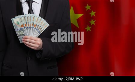 Chinesischer Geschäftsmann zeigt 100 US-Dollar-Scheine vor chinesischer Flagge Stockfoto