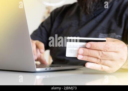 Mit Kreditkarte, mit der Hand des Mannes mit der Kreditkarte und der Tastatur des Laptops. Kaukasischer Mann, der online einkauft. Eingeben von Kreditkarteninformationen. Stockfoto