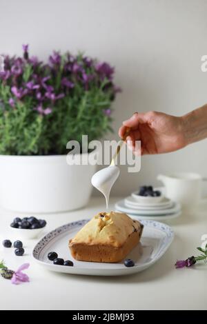 Frau, die den gebumpften Kuchen mit Glasur dekoriert, Nahaufnahme der Hand, die den Kuchen schmückt. Stockfoto