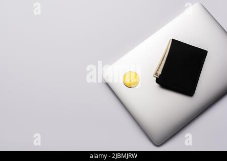 KIEW, UKRAINE - 26. APRIL 2022: Draufsicht auf Bitcoin und Brieftasche auf Laptop auf grauem Hintergrund Stockfoto