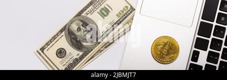 KIEW, UKRAINE - 26. APRIL 2022: Draufsicht auf goldenem Bitcoin auf Laptop in der Nähe von Dollars auf weißem Hintergrund, Banner Stockfoto