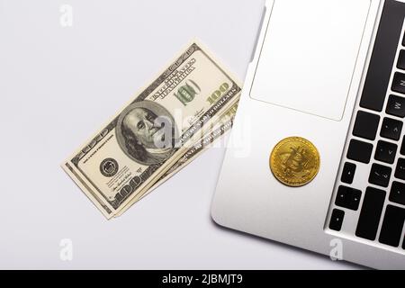 KIEW, UKRAINE - 26. APRIL 2022: Draufsicht auf Dollar in der Nähe von Bitcoin auf Laptop auf weißem Hintergrund Stockfoto