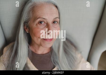 Nahaufnahme einer älteren Frau, die im Sessel sitzt und die Kamera anschaut. Stockfoto
