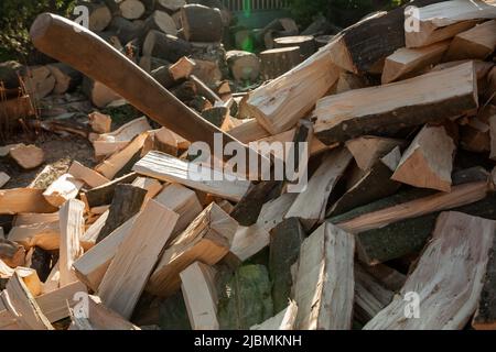 Eine Axt ragt in einem Deck hervor. Ein Stapel gehacktes Brennholz für den Ofen. Landwirtschaft Stockfoto