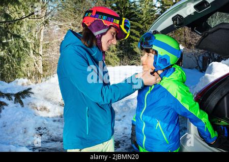 Mutter helfen jungen Snowboarder Skihelm schnallen Stockfoto