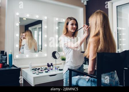 Kaukasische Kosmetikerin, die Freizeitkleidung trägt, engagiert sich für die Anwendung von Make-up auf junge weibliche Kundin im Schönheitsshop. Stockfoto