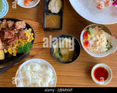 Verschiedene Menüs, Sushi, Sashimi, Nigiri, gebratenes Schweinefleisch und Miso-Suppe. Sashimi, Chutoro Sashimi, japanische Essstäbchen und Wasabi auf dem schwarzen Tisch, Stockfoto