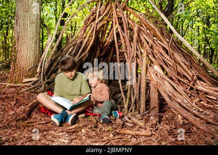 Zwei Kinder, Jungen lesen Buch, sitzen in der Hütte der Zweige Stockfoto