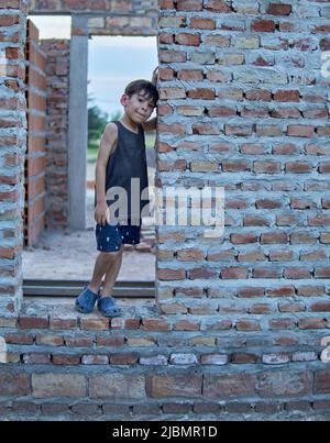 lateinischer kleiner Junge, der im Sommer in der Tür des im Bau befindlichen Hauses posiert Stockfoto