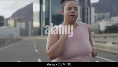 Nahaufnahme einer Frauenstadt mit gemischtem Rennen, die beim Outdoor-Workout auf der Autobahn läuft. Plus Größe Frau beginnt eine Reise zur Gewichtsabnahme und konzentriert sich auf die Gesundheit Stockfoto