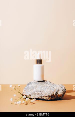 Weiße Serumflasche auf Naturstein mit Gipsophila-Blüten auf neutralem beigen Hintergrund, Nahaufnahme. Stockfoto