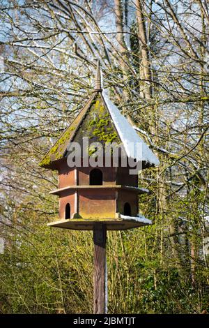 Sechseckiges Vogelhaus und Futterhäuschen aus Holz mit Frühlingsschnee bei strahlendem Sonnenschein Stockfoto