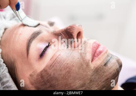 Anwendung einer Creme-Maske für Kohlenstoff-Peeling Gesicht einer erwachsenen Frau. Stockfoto