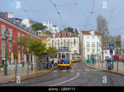 Eine traditionelle gelbe Straßenbahn, die an einer Straßenbahnhaltestelle in einer nassen Kopfsteinpflasterstraße im Zentrum von Lissabon, der Hauptstadt Portugals, steht Stockfoto