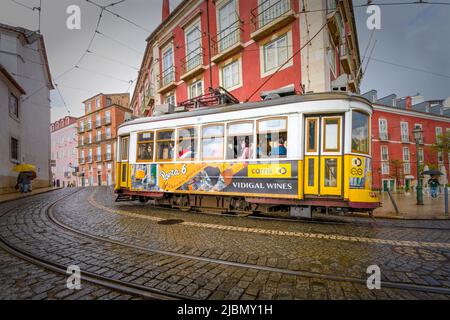 Eine traditionelle gelbe Straßenbahn fährt eine Kurve auf einer nassen gepflasterten Straße im Zentrum von Lissabon, der Hauptstadt Portugals Stockfoto