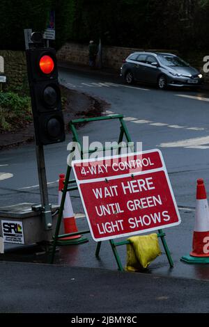 Eine Reihe von vorübergehenden Ampeln, die rot angezeigt werden. Ein Straßenschild warnt vor einer 4-Wege-Verkehrskontrolle an einer Kreuzung, um Straßenarbeiten zu ermöglichen. Stockfoto