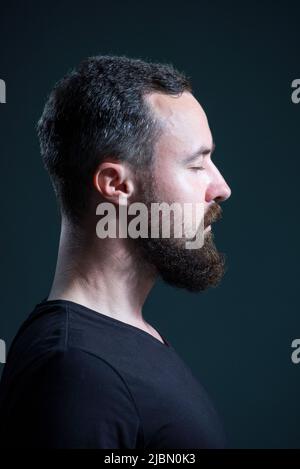 Dramatisches Porträt-Profil von tausendjährigen bärtigen Kerl auf schwarzem Hintergrund Stockfoto