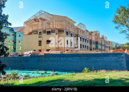 An einem hellen, sonnigen Tag wird ein neues Gehäuse gebaut, das mit einem klaren blauen Himmel, grünen Baumblättern, Gras und einer steinernen Stützmauer ausgestattet ist. Stockfoto