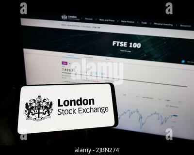 Person mit Mobiltelefon und Logo des Finanzmarktplatzes London Stock Exchange (LSE) auf dem Bildschirm vor der Webseite. Konzentrieren Sie sich auf die Telefonanzeige. Stockfoto