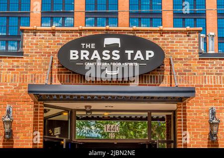 Die Außenfassade des Brass Tap Craft Beer Food and Spirits Tap Room und das ovale Logo auf einem Backsteingebäude über dem Eingang mit Glasfenstern. Stockfoto
