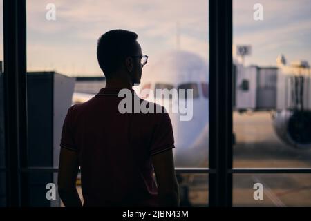 Silhouette des Menschen während des Wartens auf den Flug. Reisende, die vom Flughafenterminal aus schauen, bevor sie zum Flugzeug steigen. Stockfoto