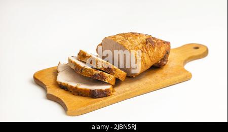 Hausgemachtes, gebackenes Schweinefilet mit Gewürzen auf einem hölzernen Küchentafel auf weißem Hintergrund Stockfoto