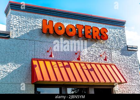 Die Marken- und Logo-Beschilderung der Hooters-Außenfassade in kräftigen, orangen Buchstaben über einer gerippten Markise aus Metall auf einem strukturierten Gebäude in hellem Sonnenlicht. Stockfoto