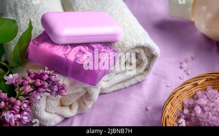 Spa- und Bad-Accessoires in violetten Tönen. Handgemachte Seife, Handtücher, Meersalz. Ein Zweig von Flieder. Stockfoto