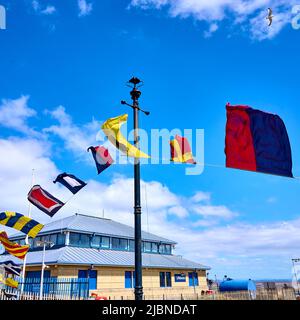 Verschiedene Flaggen, die im Wind über dem Fleetwood Fährhafen und der Rettungsbootstation wehen Stockfoto