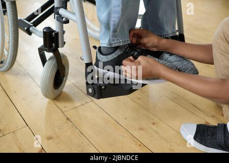 Nahaufnahme eines kleinen Jungen, der Schuhbänder auf die Schuhe seines behinderten Vaters kitzelt, während er im Rollstuhl sitzt Stockfoto