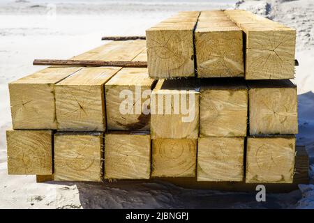 Blick vom Ende auf die gestapelten, imprägnierten quadratischen Kiefernbalken an einem Sandstrand Stockfoto