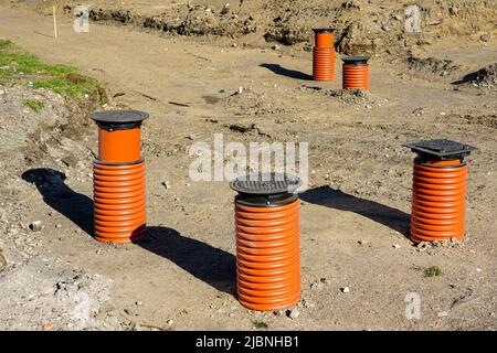 Neue Sturmwasserentwässerungsbrunnen mit schwarzer Eisenrost-Abdeckung und braunen Kunststoff-Kanalrohren auf einer neuen Straßenbaustelle Stockfoto