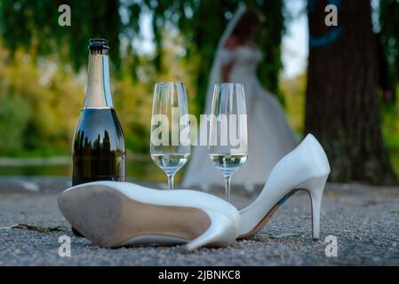 Eine Champagnerflasche, ein Paar High Heels und zwei Sektgläser befinden sich auf dem Boden im Freien, Ende einer Hochzeit Stockfoto